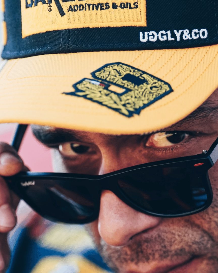 Close up of Danilo Pertrucci wearing a yellow and black Uggly&Co Bardahl Danilo Pertrucci #9 merchandise trucker hat