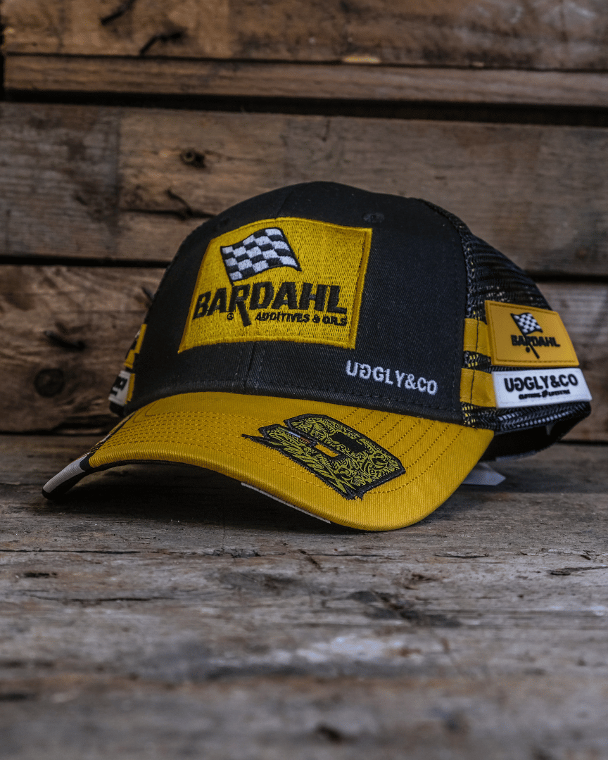 Yellow and black Uggly&Co Bardahl Danilo Pertrucci #9 merchandise trucker hat on a wooden surface