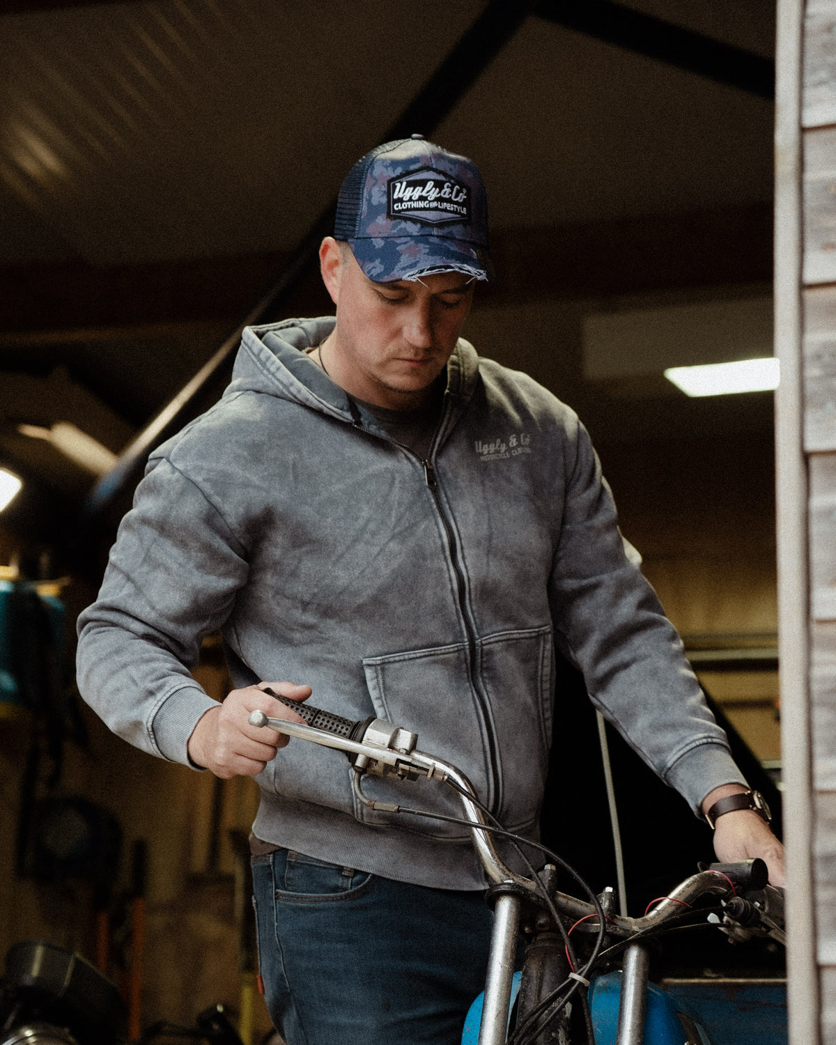 Blue camo trucker hat worn by mechanic working on a vintage motorbike