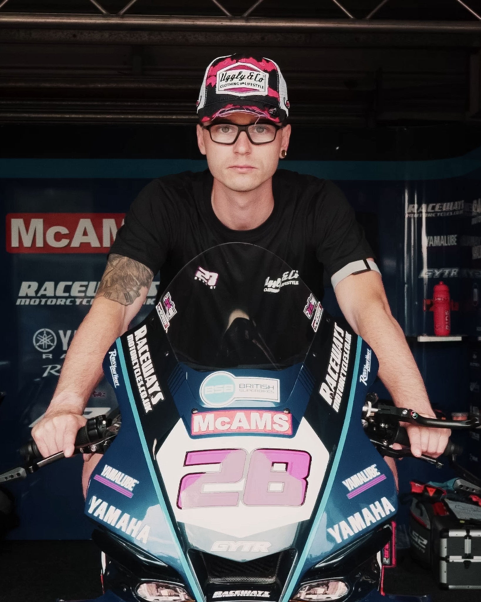 Bradley Ray seen wearing a pink black and white trucker hat whilst sat on his mcams bike