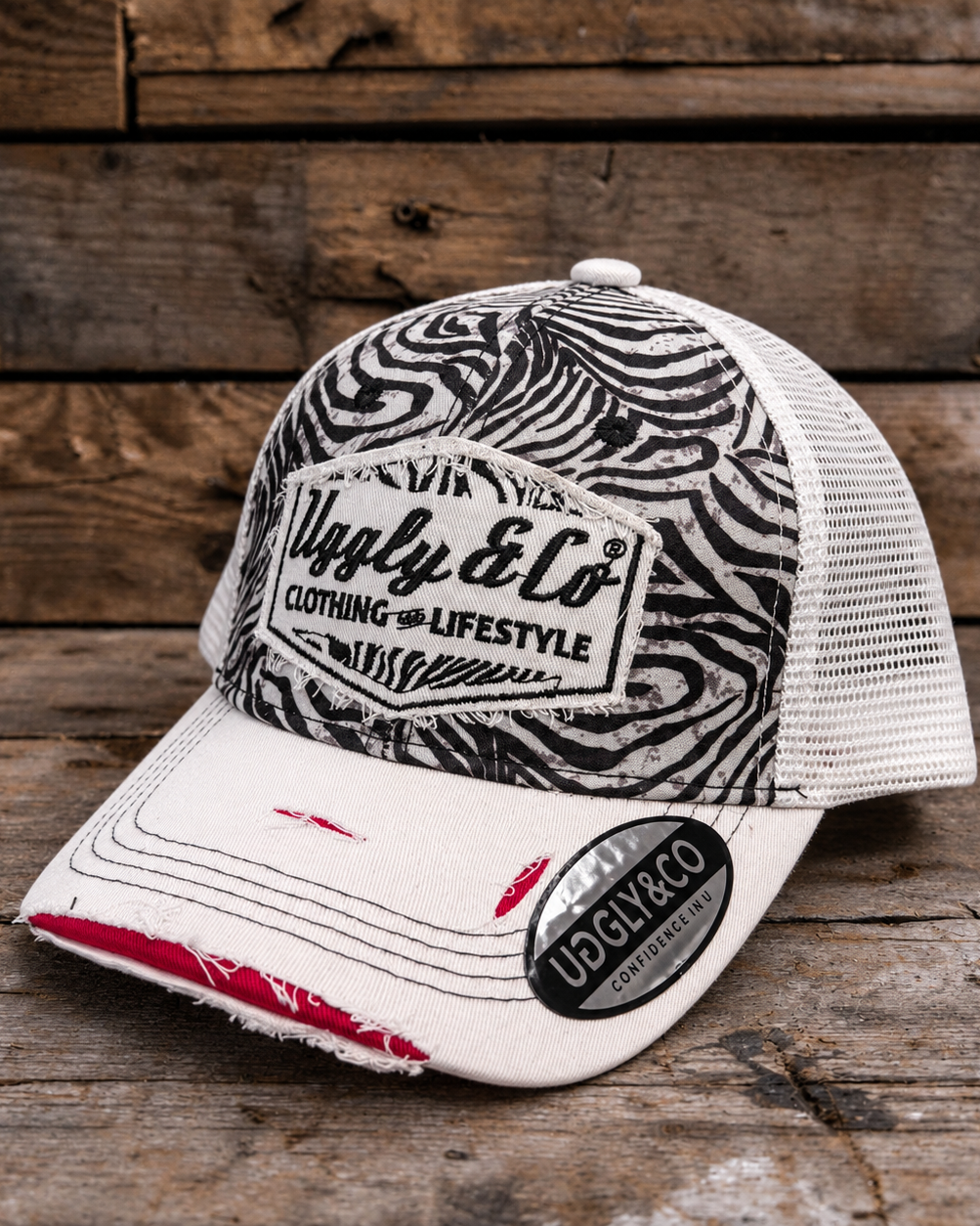 A trucker-style cap with a black and white zebra-patterned front panel, white mesh back, and a white brim with distressed edges and red stitching. The front patch reads 'Ugly & Co Clothing and Lifestyle.