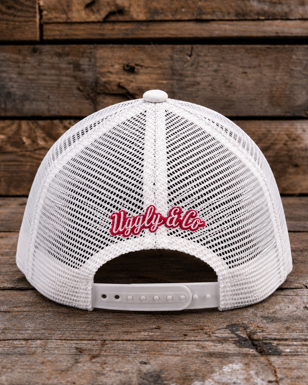 White mesh trucker hat shown from the back, featuring red embroidered cursive text reading 'Ugly & Co.' on the center back, photographed against a rustic wooden plank background.