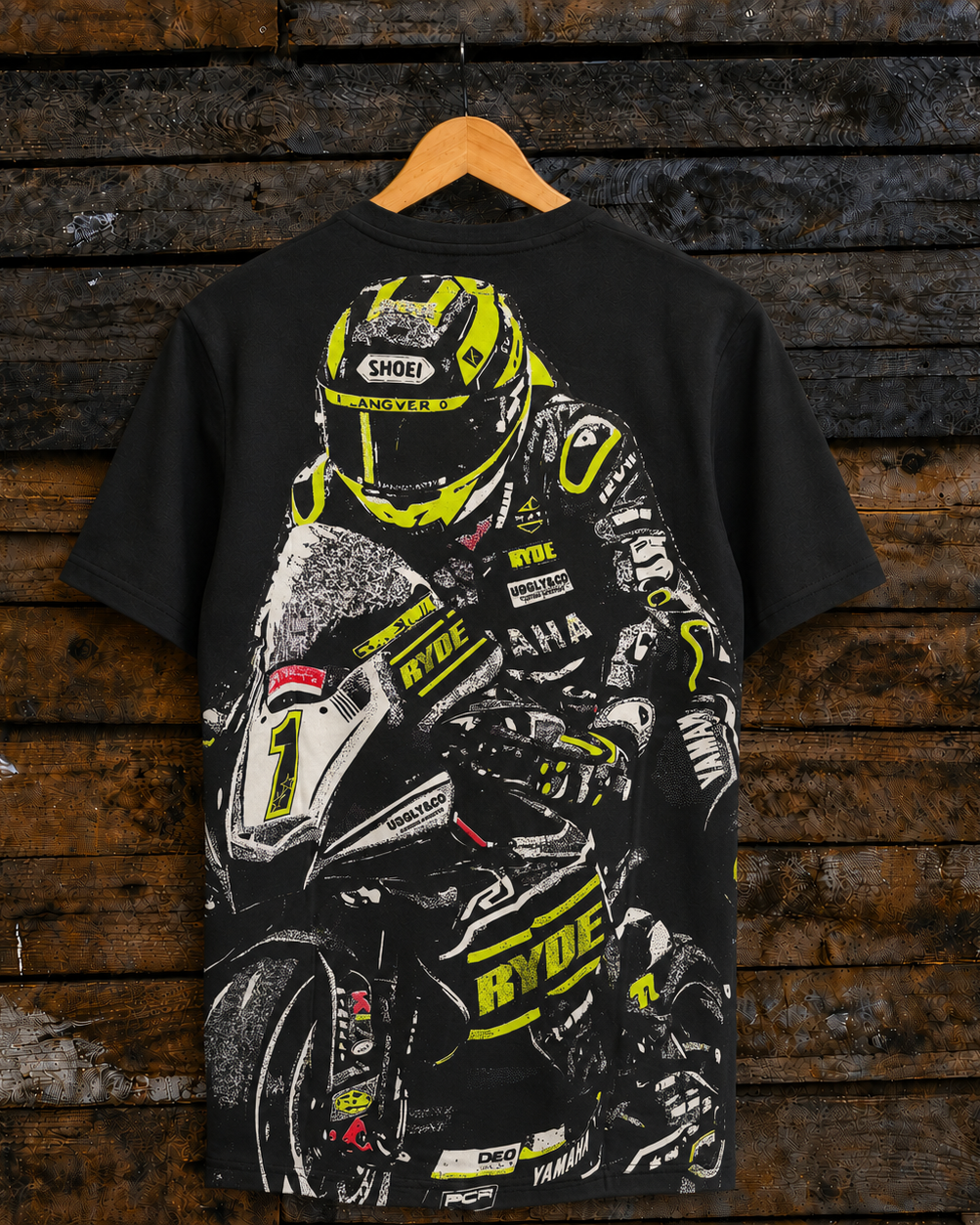 Rear view of a black t-shirt with a graphic of motorcyclist Kyle Ryde and brand logos, hanging on a rustic wooden wall.