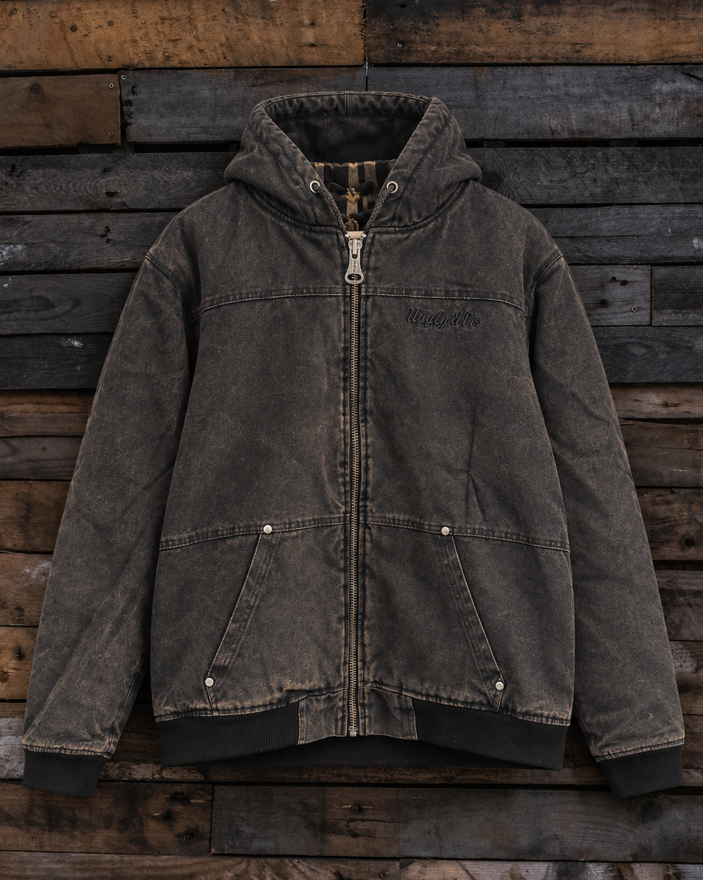 A dark gray washed canvas hooded jacket with a front zipper, displayed flat against a rustic wooden plank background.