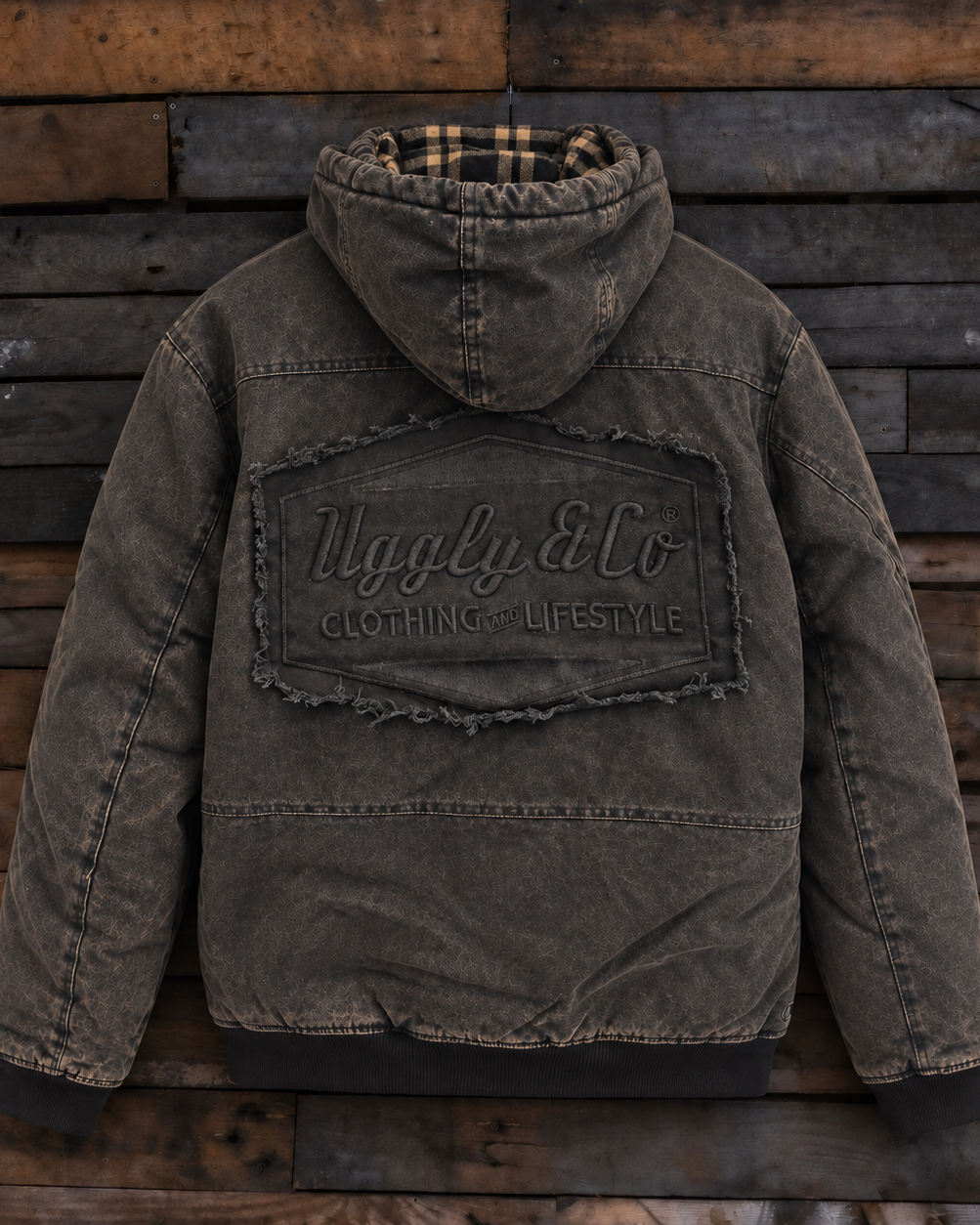 A washed dark brown hooded puffer jacket with a large distressed patch on the back reading 'Uggly & Co Clothing Lifestyle,' displayed against a rustic wooden plank background.
