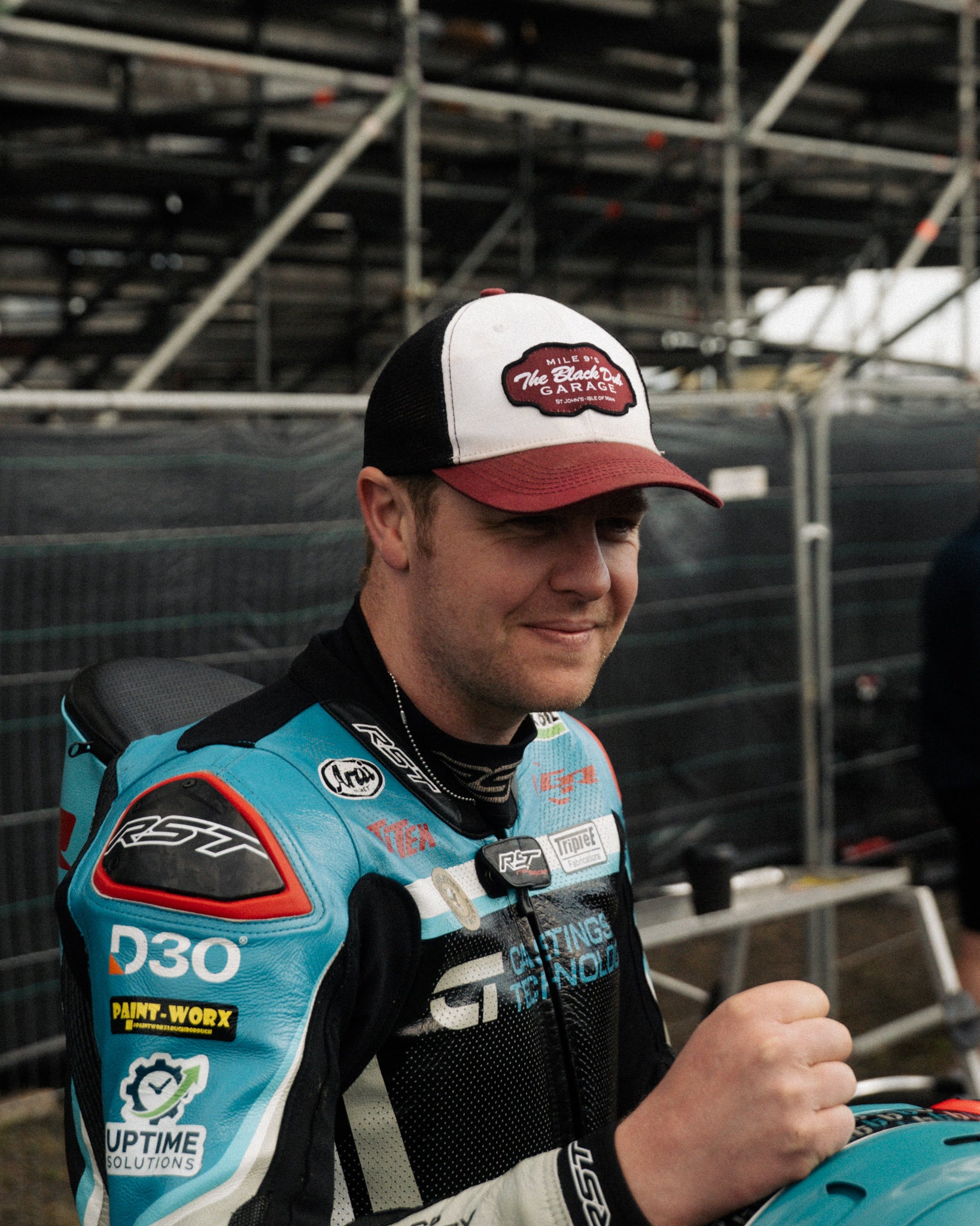 Dan Ingham in black dub hat by pit lane and race stands from side profile