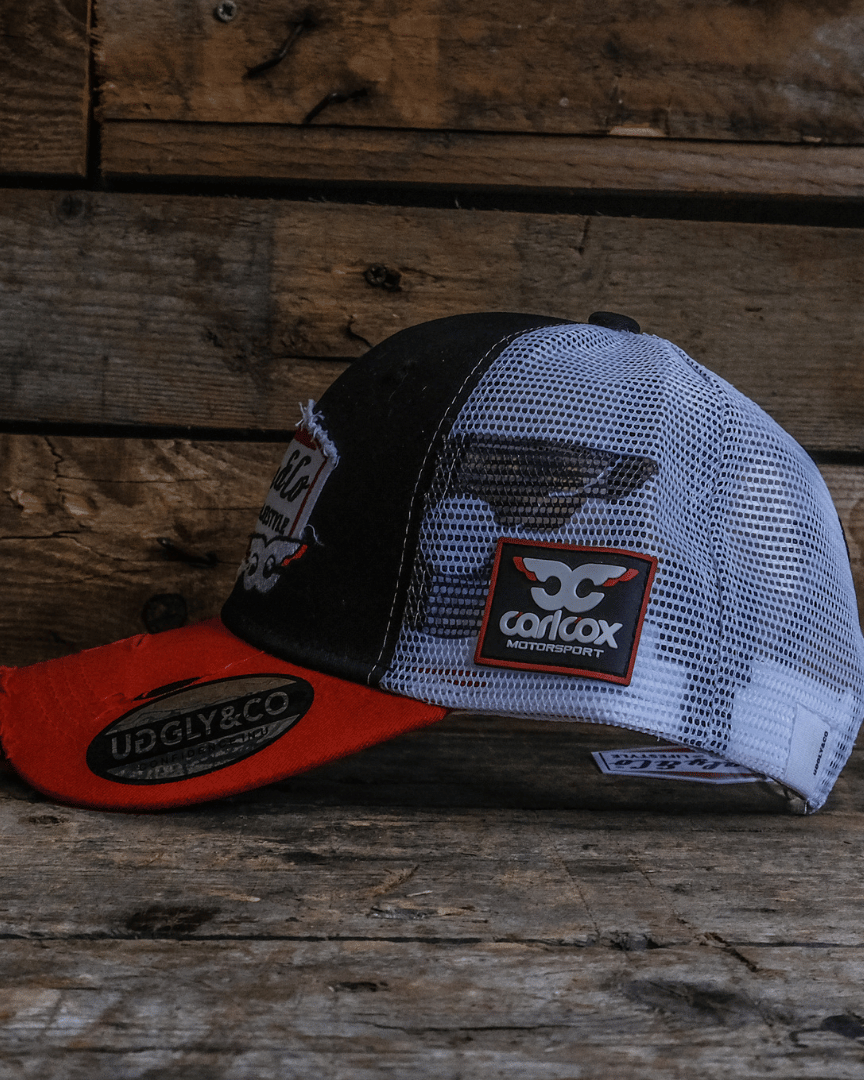 Trucker hat with red brim, black and white mesh back, and visible branding on a wooden surface.