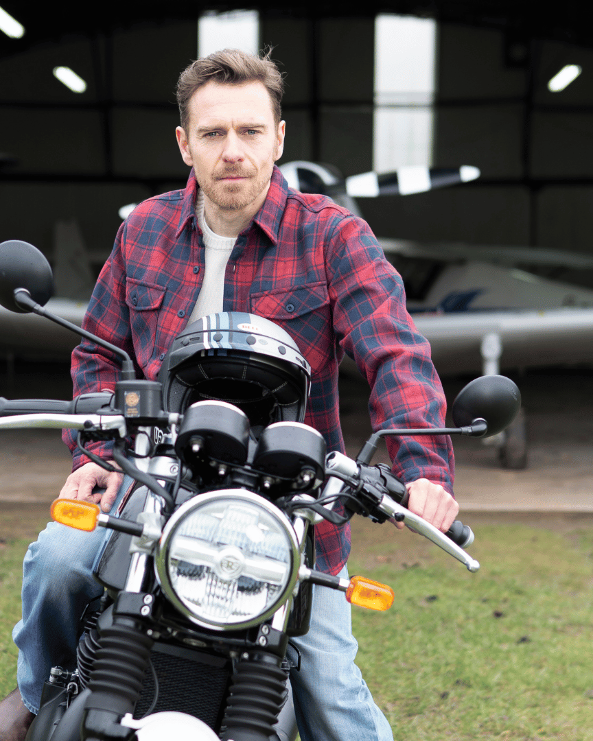 Man in a red plaid shirt sitting on a motorcycle with airplanes in the background