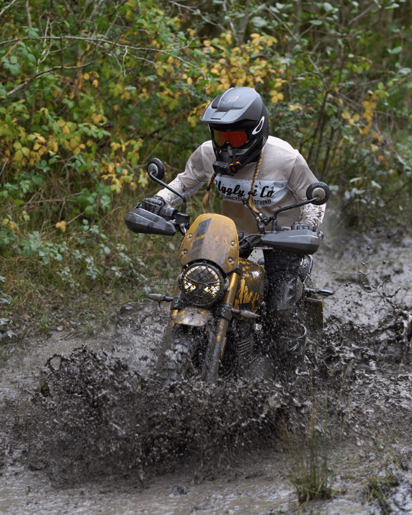 Riding through muddy puddles in a long-sleeve motocross jersey with 'Uggly & Co Motorcycle Clothing' logo