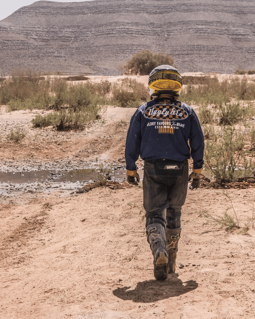 MX rider walking in the desert in a blue Uggly&Co motocross jersey
