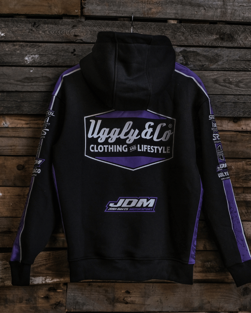 A black hoodie with purple and white highlights, featuring the Uggly&Co logo and the text 'JDM' on a wooden background.