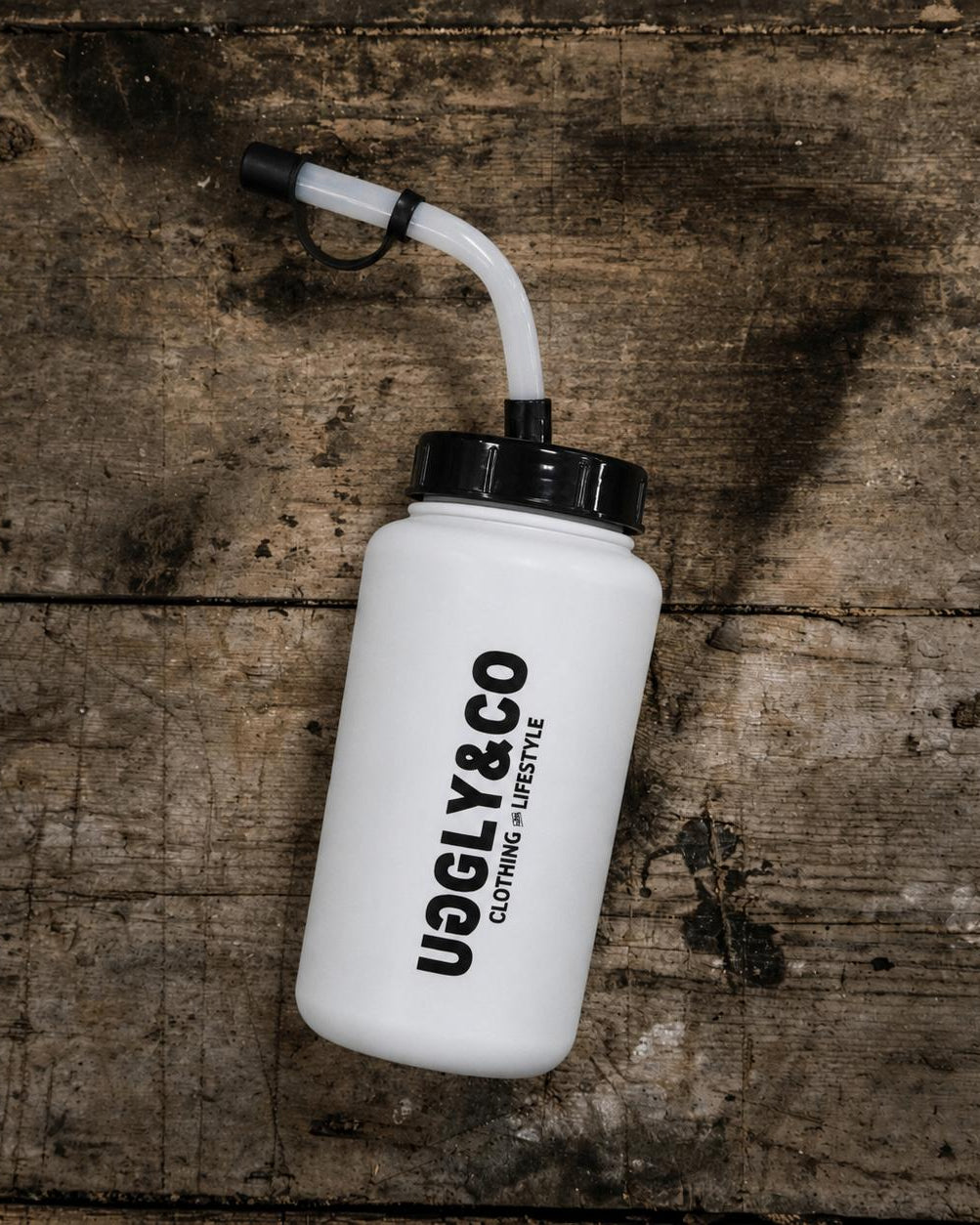 White water bottle with black cap and 'Uggly&Co' branding on a wooden surface
