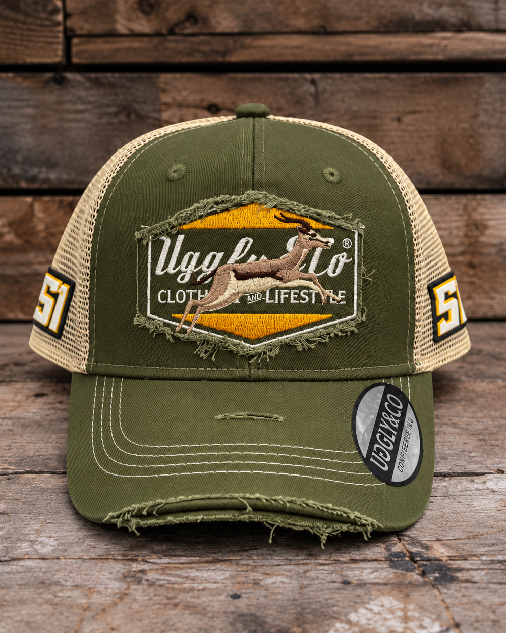 An olive green and beige trucker-style baseball cap with a distressed, frayed look, featuring a large embroidered patch on the front with a deer graphic and the text 'Uggly & Co'. The side panels have '51' printed on them, and a 'Clothing & Lifestyle' sticker is visible on the brim, set against a rustic wooden background.