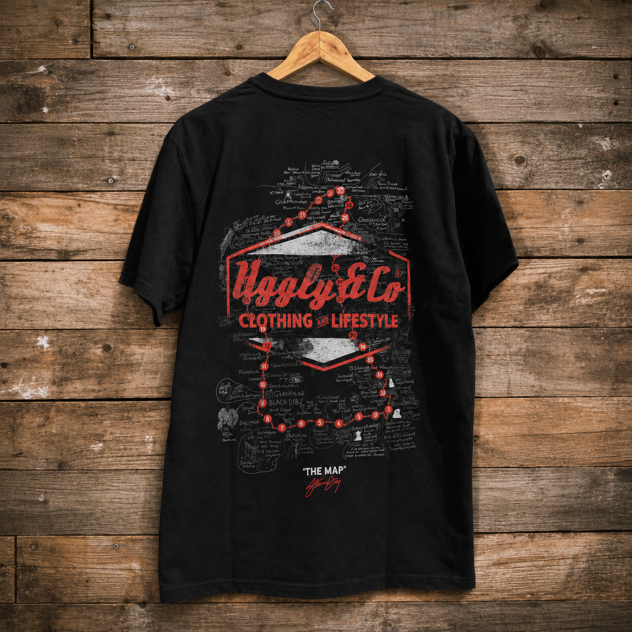 Rear view of an Uggly&Co black t-shirt with commentator Steve Day The Map graphic on the back featuring authentic Isle of Man TT notes on a wooden background