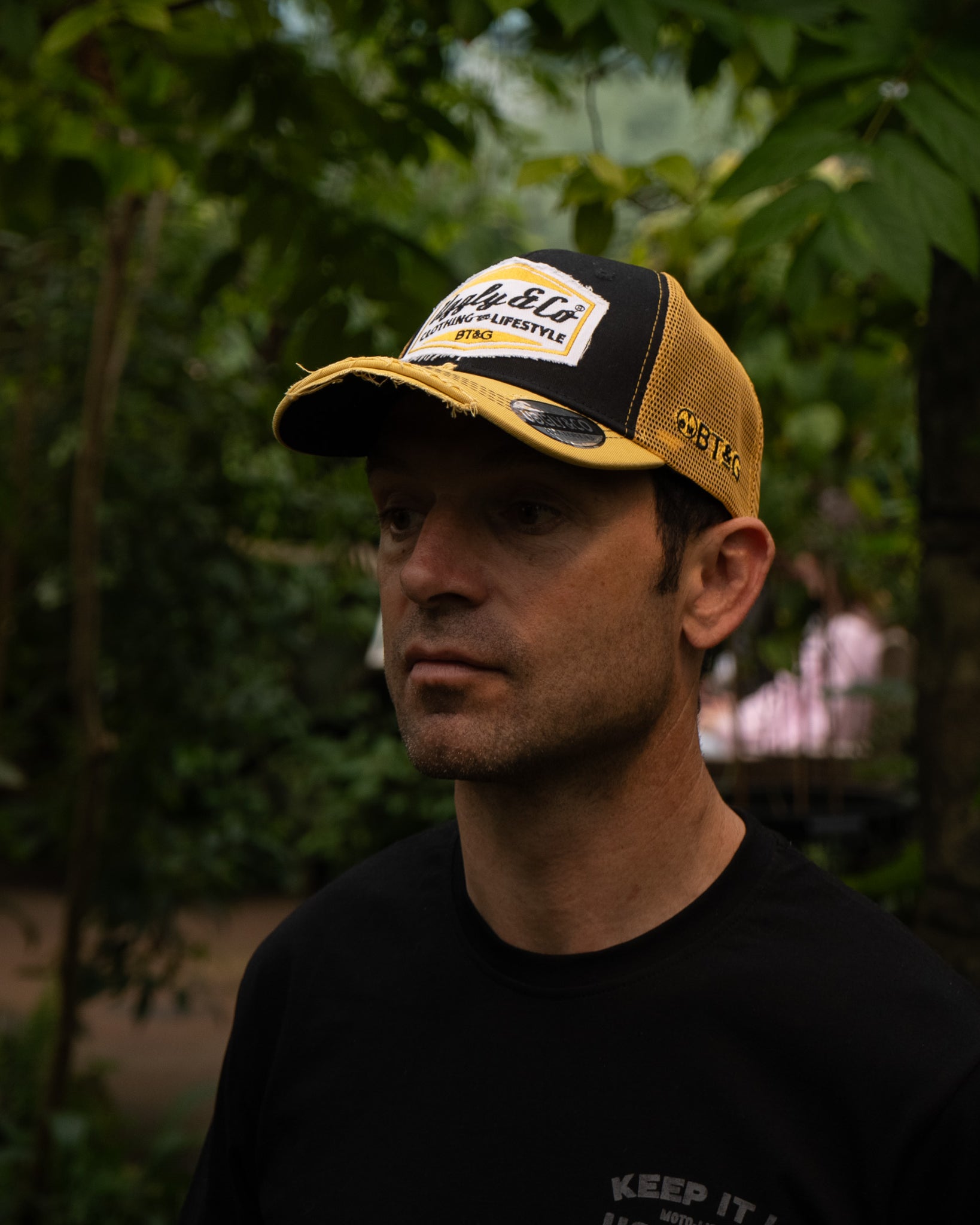 Sylvain Guintoli in the butchers tap trucker hat stood in forest
