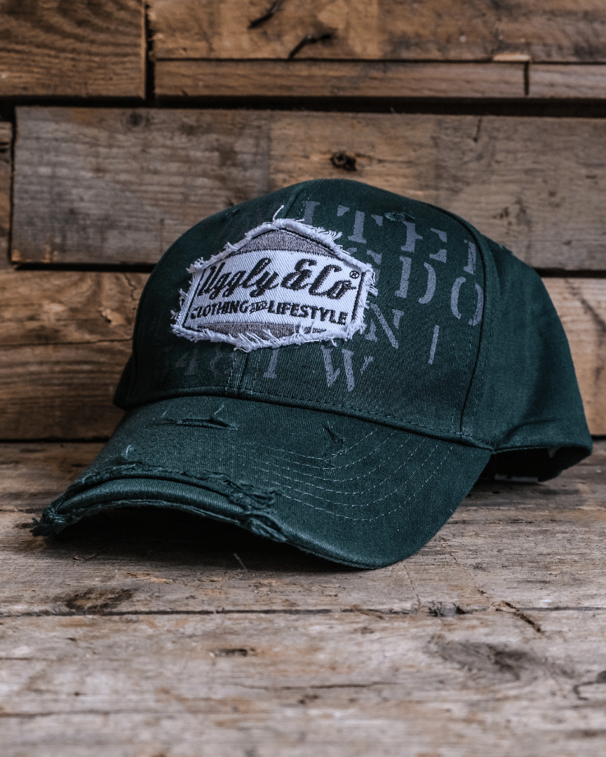 A green 'Aviation' Diamond Trucker Hat with distressed black and white Uggly&Co logo, placed on a wooden surface.