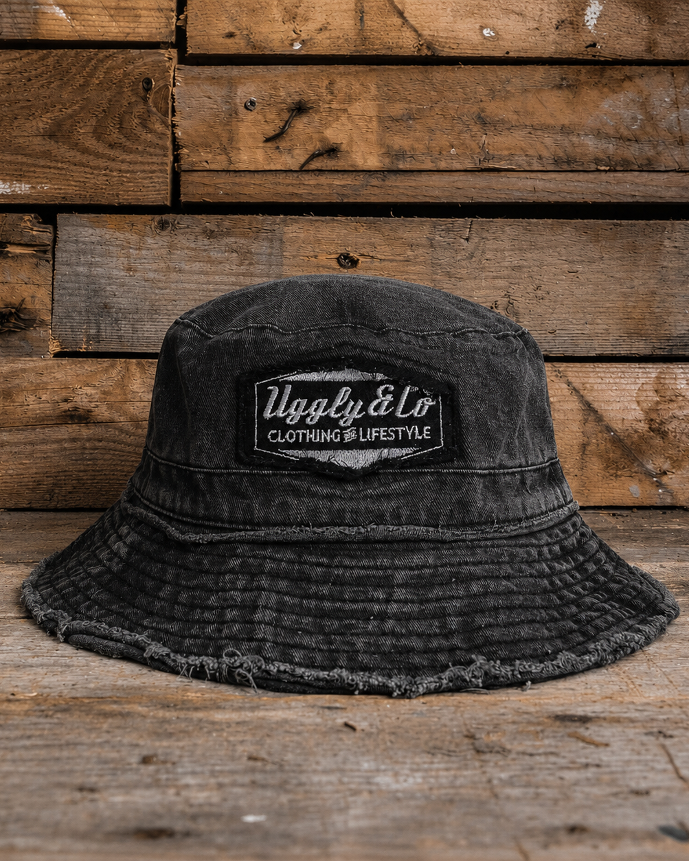 Acid washed distressed black bucket hat with an Uggly&Co logo on a wooden background