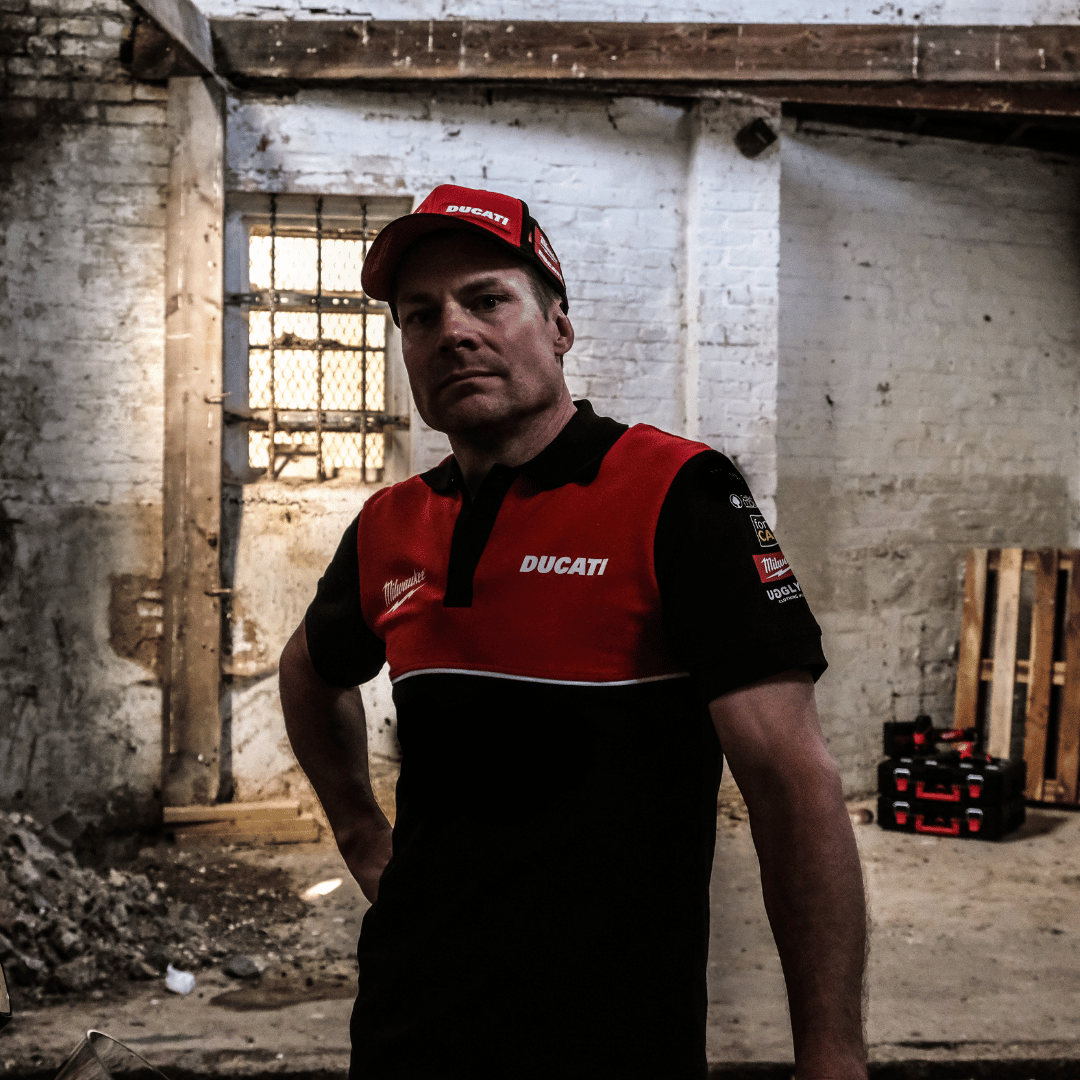 A model looking at the camera while wearing a Milwaukee x Ducati polo shirt, featuring a black lower half and a red upper torso in a warehouse