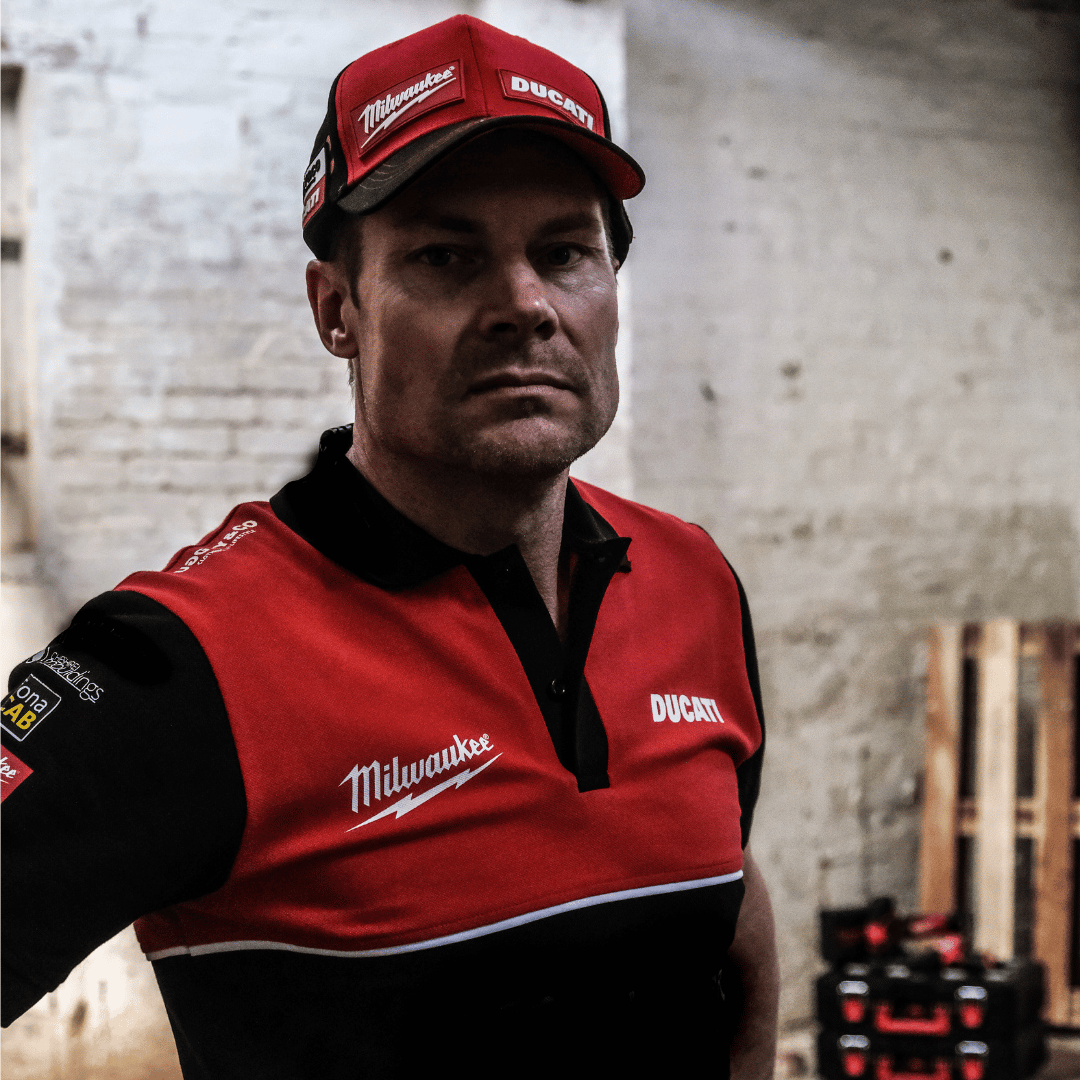A model looking straight at the camera while wearing a Milwaukee x Ducati polo shirt, featuring a black lower half and a red upper torso in a warehouse