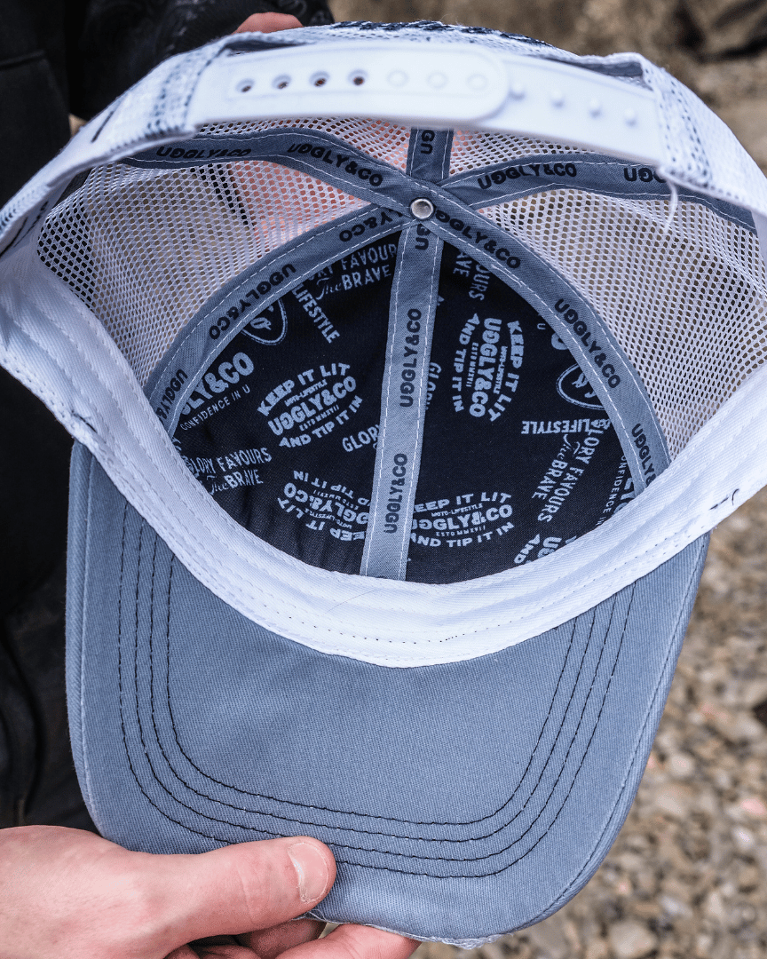 The inside of a trucker hat with Uggly&Co branding along the seams with a blurred rocky background