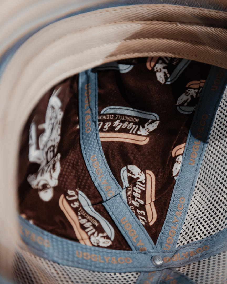 Inside view of a dusty blue, white and brown trucker hat with with Uggly&Co branding on the seams