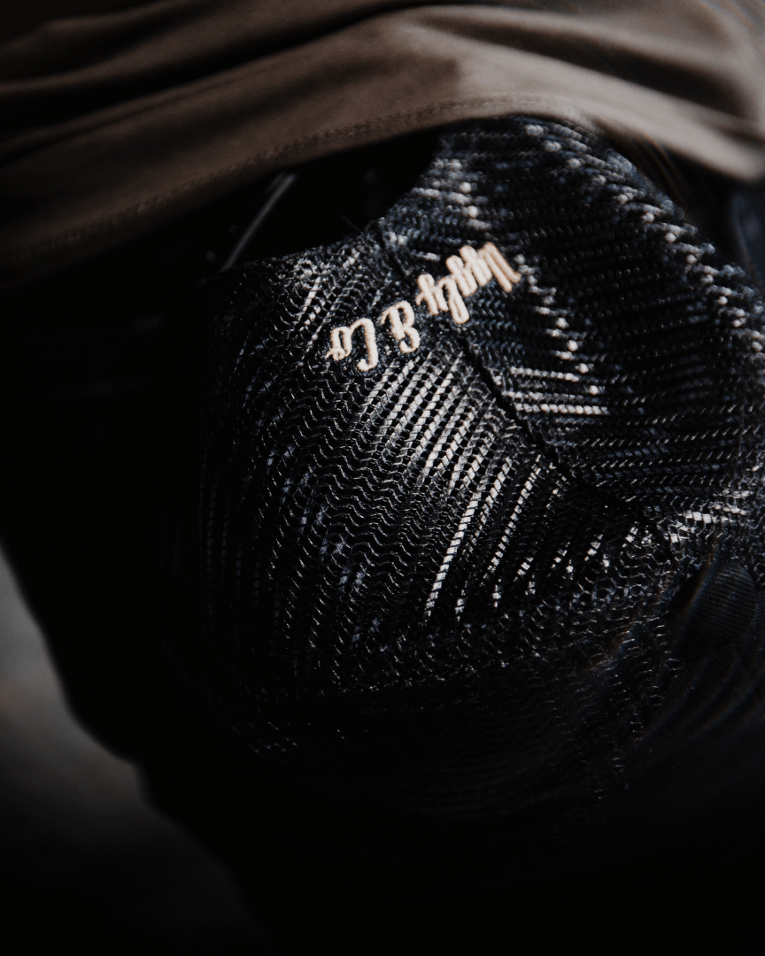 Abstract view of an all-black trucker hat with a vintage-inspired flat track racing logo in yellow and blue on the front at night