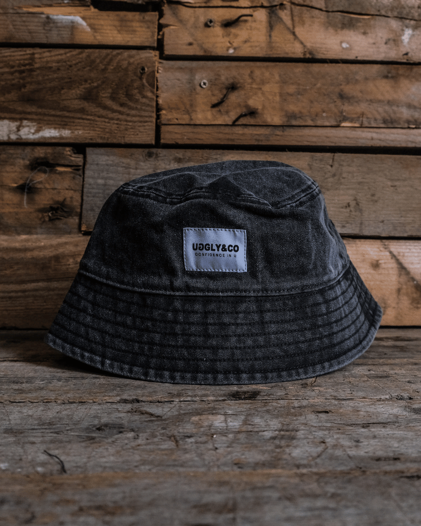 Vintage black bucket hat with an Uggly&Co brand label on a wooden background