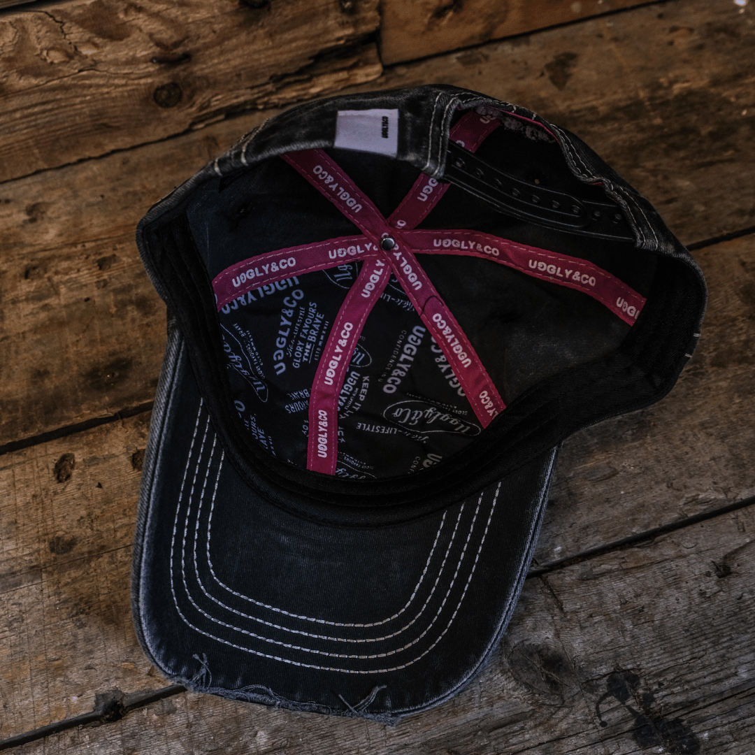 Inside view of a black trucker hat with Uggly&Co branding on the seams, set against a vintage wooden background.