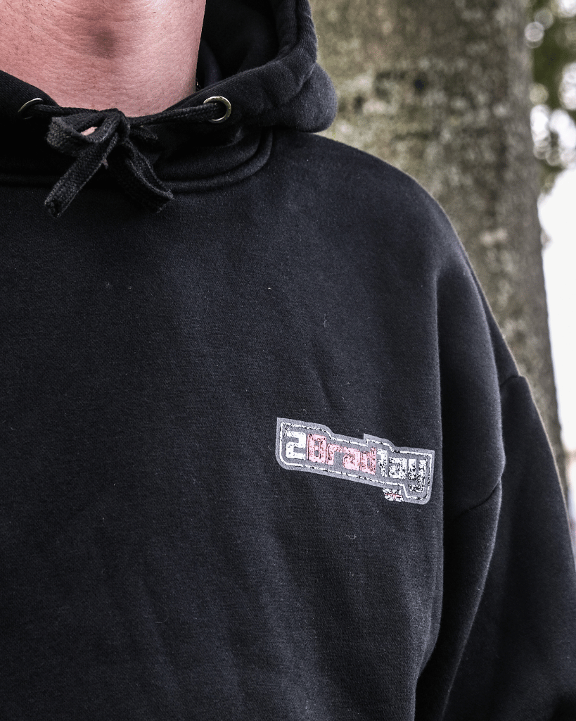 Black hoodie with a logo on the chest worn by a person, outdoors.