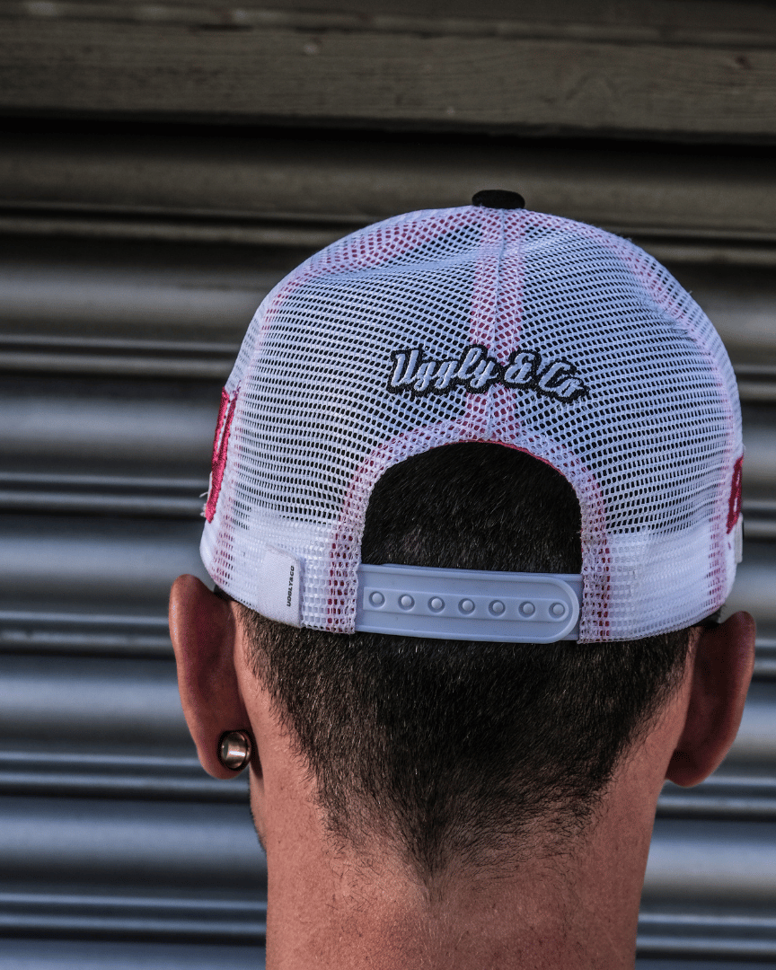 Back view of Bradley Ray wearing a trucker hat with Uggly&Co branding, standing against a garage roller door