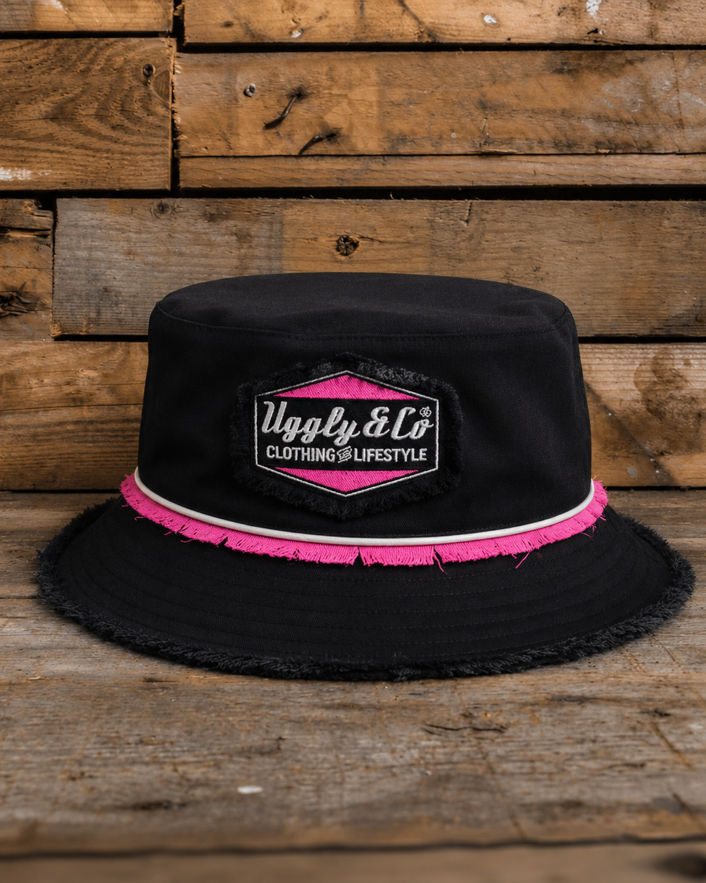 Black bucket hat with pink trim and visible brand logo on a wooden background