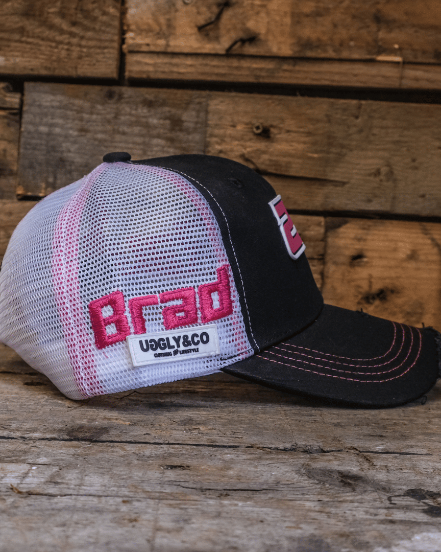 Side view of a trucker hat with 'Brad' and the Uggly&Co logo on the side in front of a wooden background