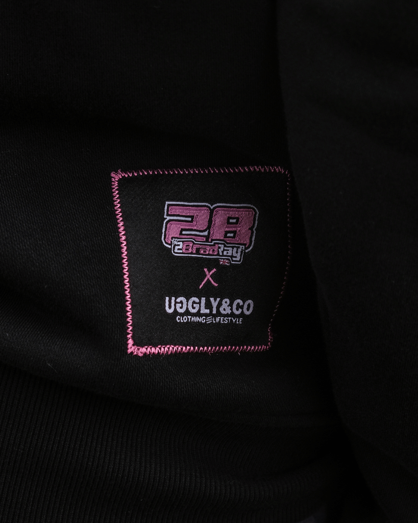 Close-up of a black garment with a brand label featuring '28' and 'UGLY&CO'.
