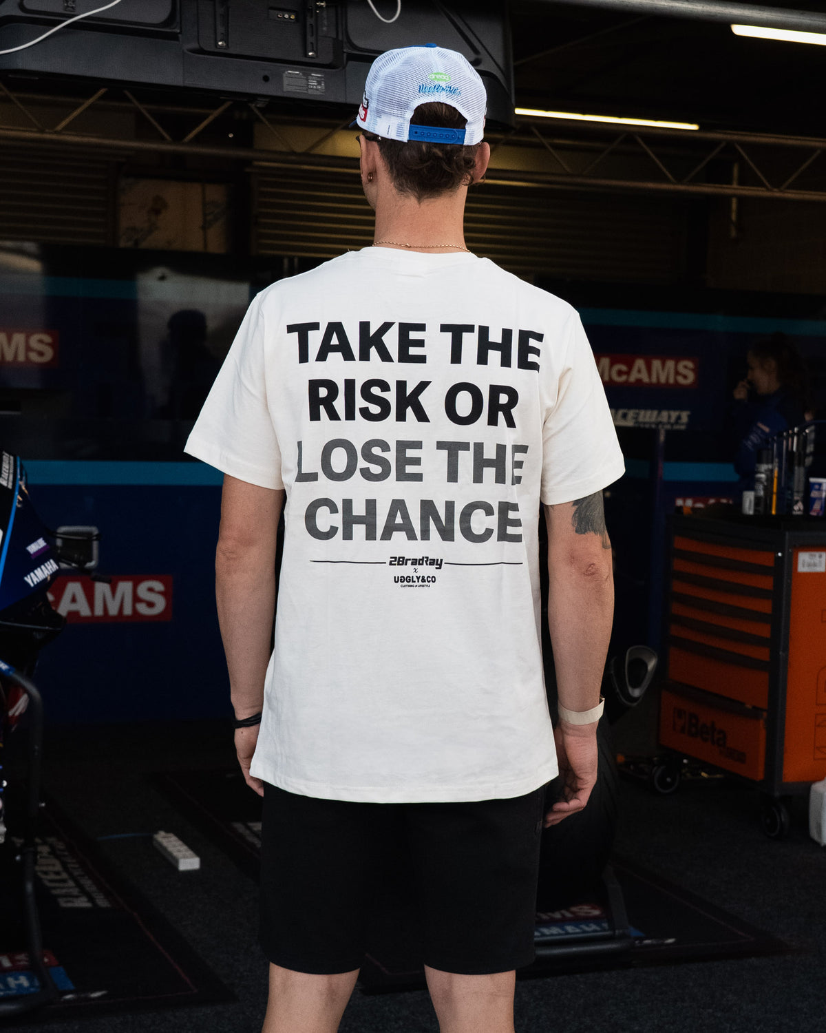 Bradley Ray wearing White 'Take the Risk' T-Shirt in a McAMS Yamaha motorcycle garage setting
