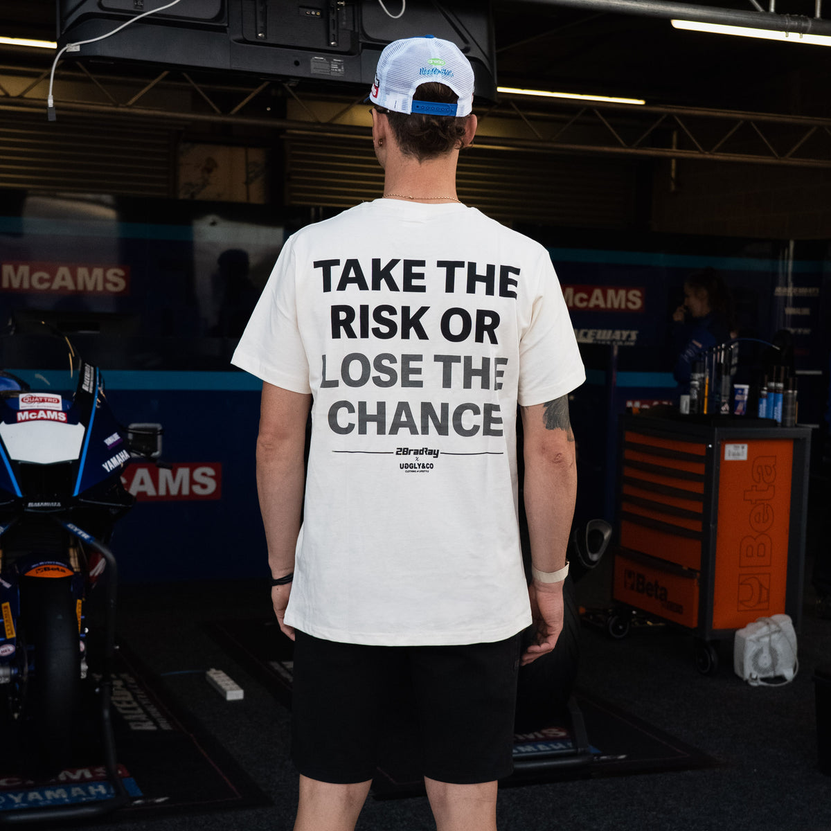 Bradley Ray wearing White 'Take the Risk' T-Shirt in a McAMS Yamaha motorcycle garage setting