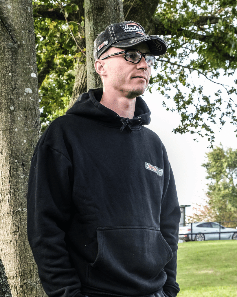 Brad Ray wearing a black hoodie and cap standing outdoors with trees in the background
