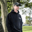 Brad Ray wearing a black hoodie and cap standing outdoors with trees in the background