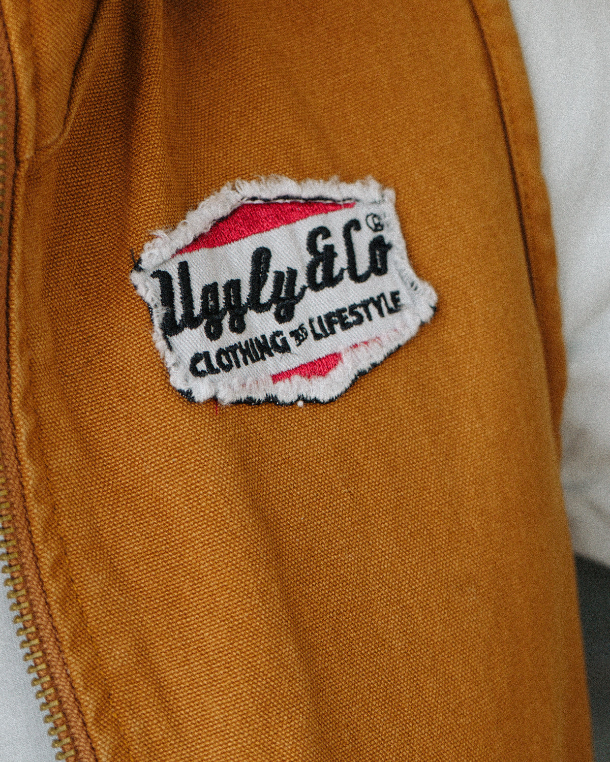 Close up of the Uggly & Co logo detail on the Brown Workwear Canvas Gilet, highlighting the branding and durable canvas material of this motorcycle lifestyle workwear piece.