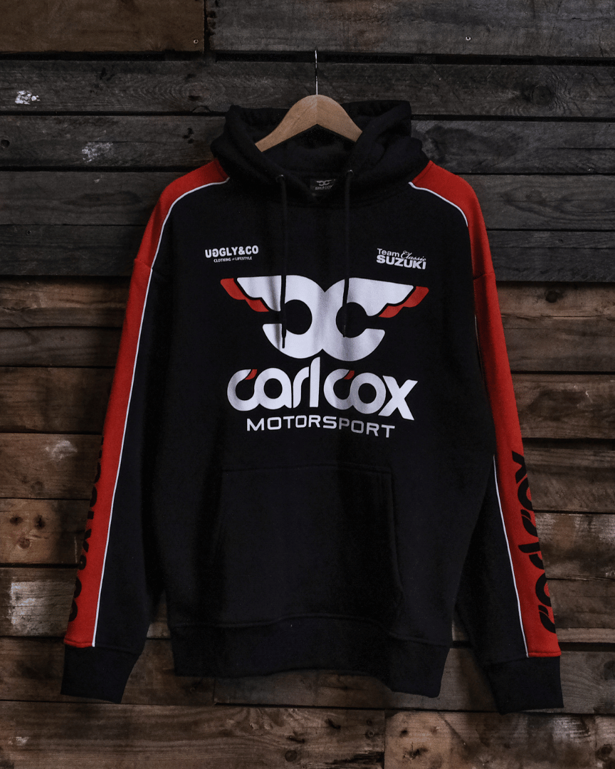 Black hoodie with red sleeves featuring Carl Cox Motorsport branding on a wooden background