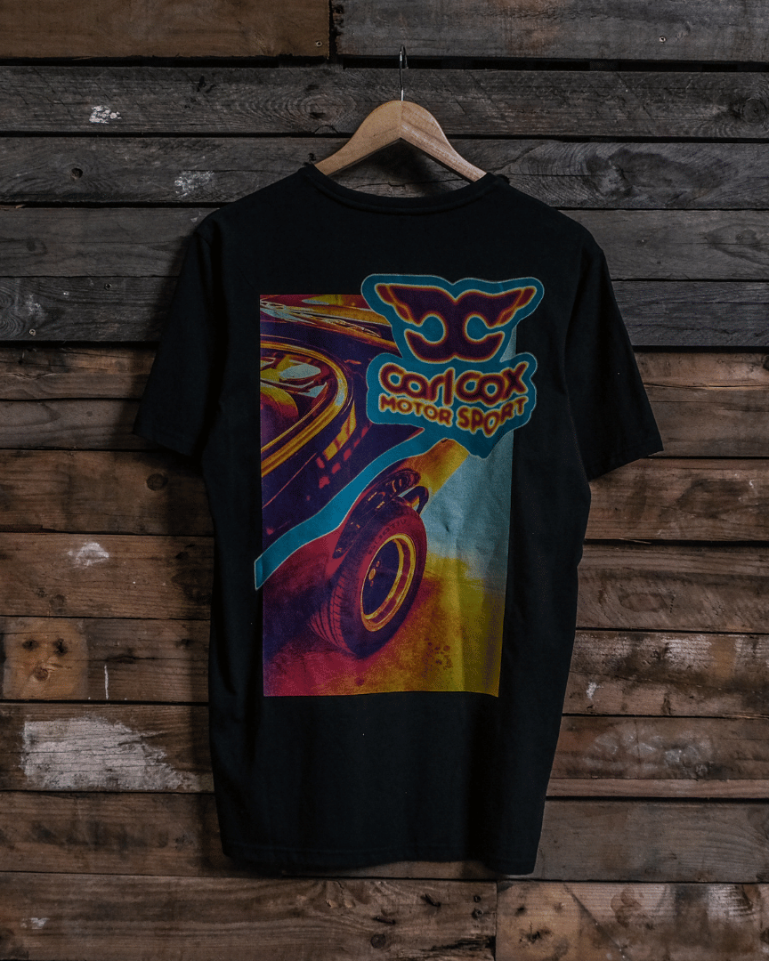 Rear view of a Carl Cox motorsport black t-shirt with a colourful graphic design on a wooden wall