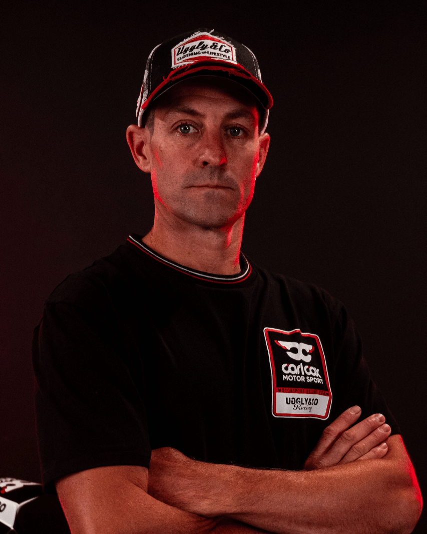 A model wearing a Carl Cox motorsport black t-shirt with an Uggly&Co logo looking at the camera