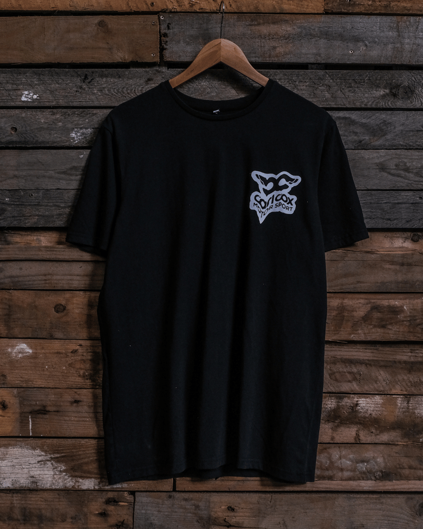 Front view of a Carl Cox Motorsport black t-shirt with car graphic and 'carl cox motorsport' logo on a wooden background