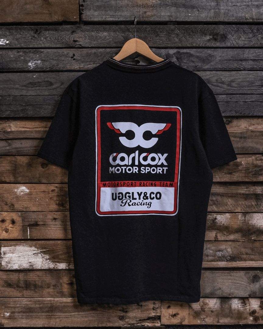 Rear view of a Carl Cox motorsport black t-shirt with an Uggly&Co logo on a wooden background