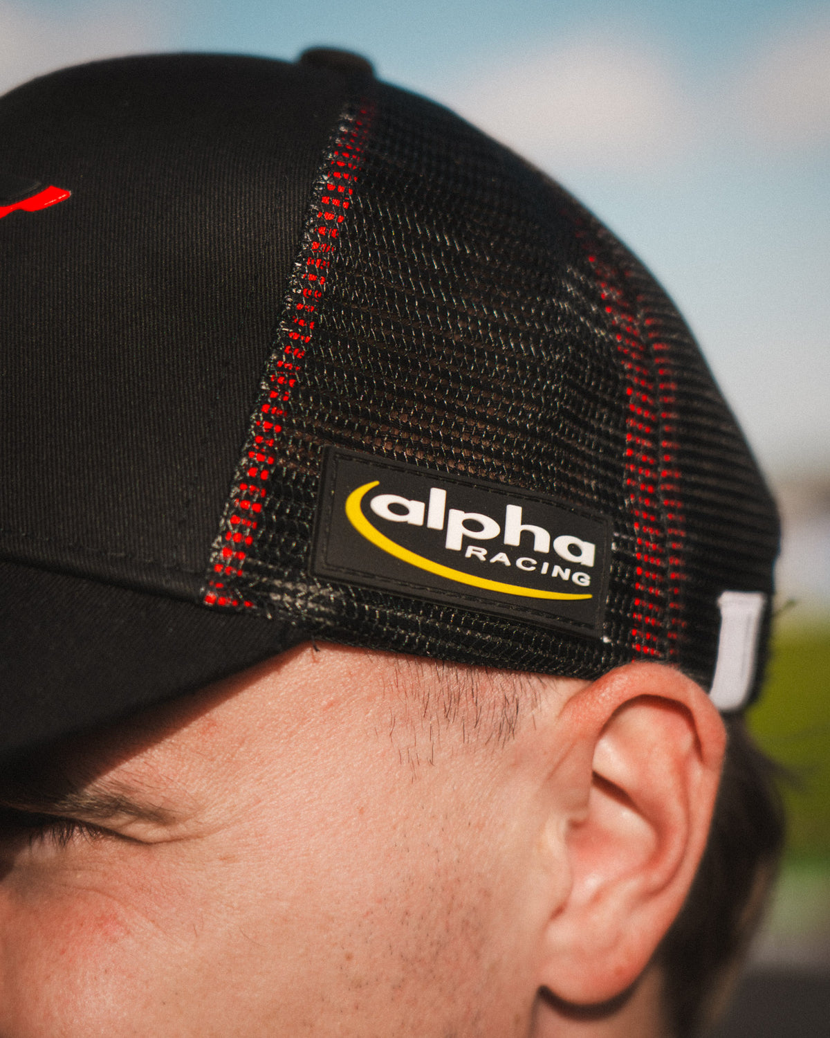 Side profile of the Carl Cox x Alpha Racing & Simon Reid Trucker Hat, showcasing its alpha racing logo