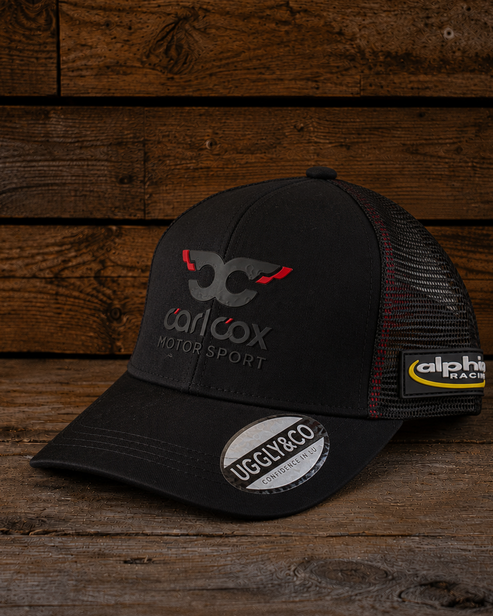 Carl Cox Trucker Hat x Alpha Racing & Simon Reid shown from the front with black panels, motorsport branding and a classic trucker fit.