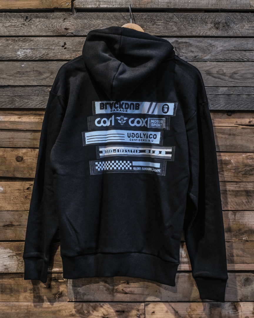 A black zip hoodie with text and graphic logos on the back, displayed against a wooden background.