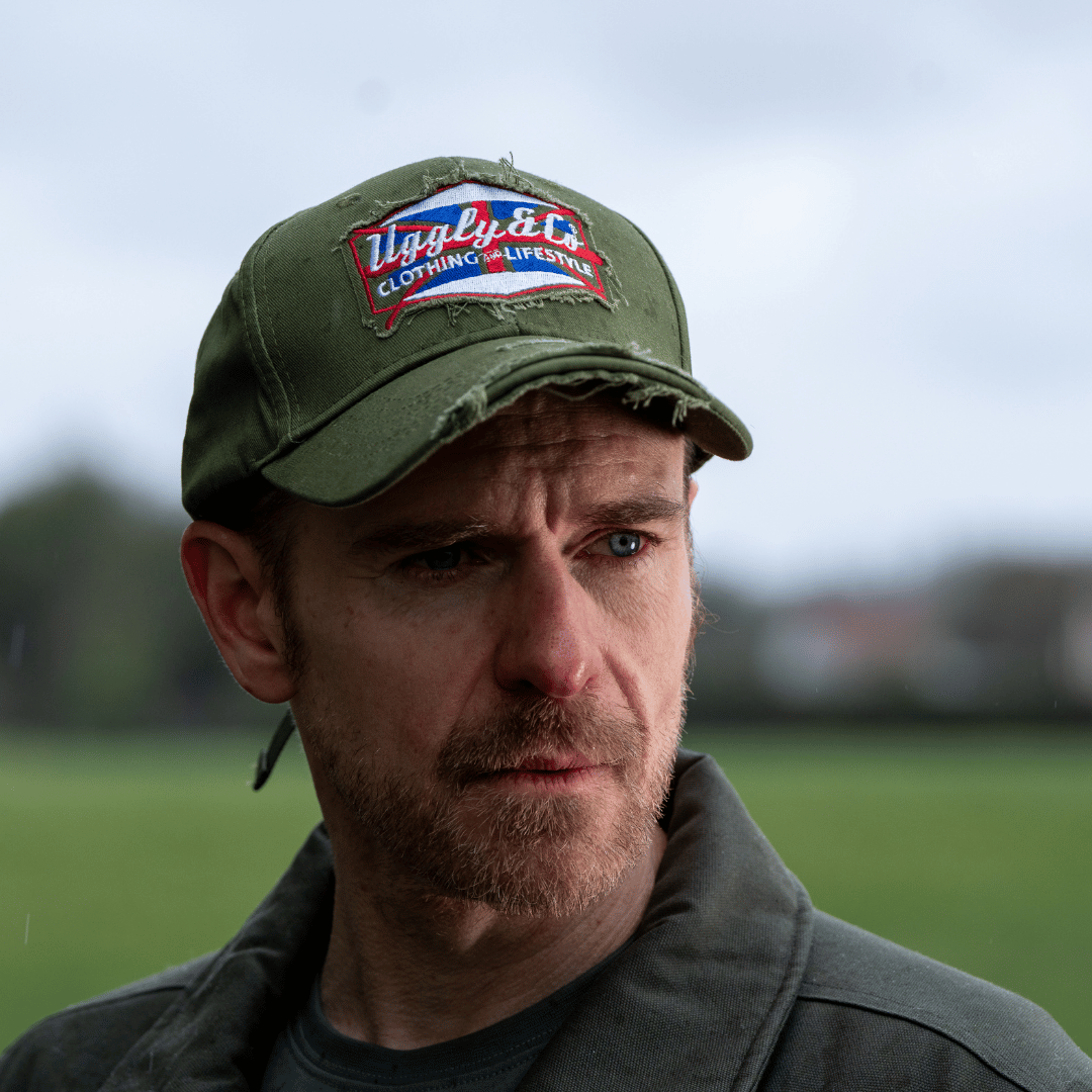 A model wearing a green vintage cap with a union jack Uggly&Co brand logo with a blurred background