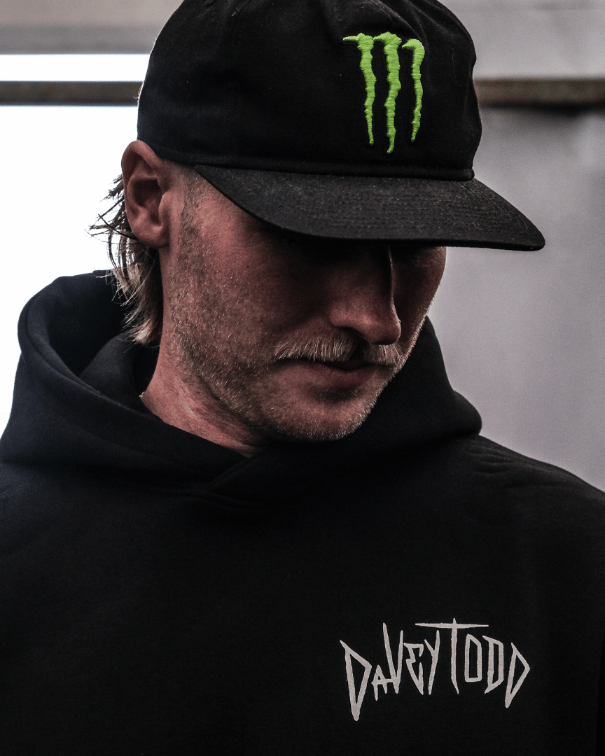 Person wearing a black hoodie with 'Davy Todd' logo and a black cap with a green logo.