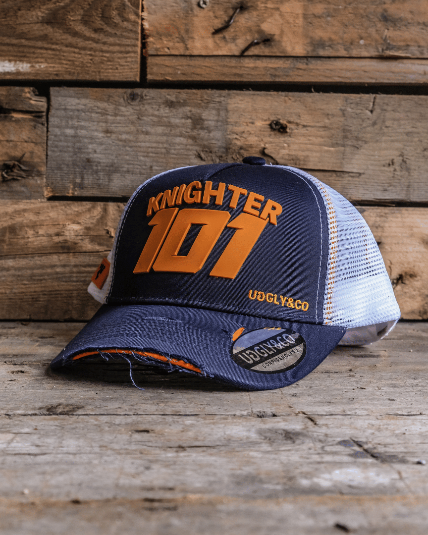 A navy blue and orange trucker hat with 'KNIGHTER 101' text on the front, featuring a breathable nylon mesh back and a curved peak. The cap is placed on a wooden surface.