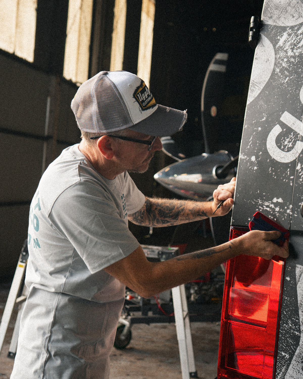 Grey & White Diamond Trucker Cap worn during a van wrapping session inside a hangar.